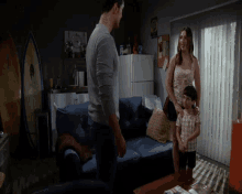 a man standing next to a woman and a boy in a living room with a surfboard in the background
