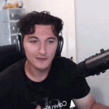 a young man wearing headphones and a black shirt is sitting in front of a microphone .