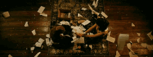 two people are sitting on the floor with papers flying around them