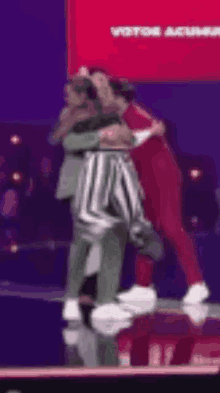 a couple of people are hugging each other on a stage in front of a red sign .