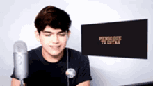 a young man is sitting in front of a microphone with a sign that says " pienso que tu estas " behind him