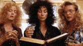 three women are looking at a book and drinking
