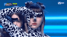 a woman in a black and white leopard print outfit stands in front of a mnet banner