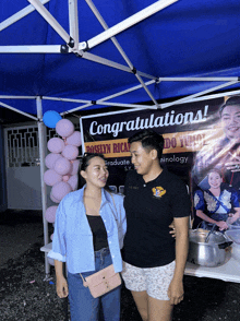 a man and a woman are standing in front of a tent that says congratulations