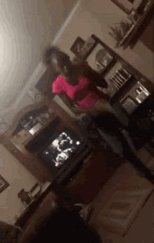 a woman in a pink shirt is dancing in a living room