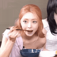 a woman with red hair is eating a bowl of food with chopsticks