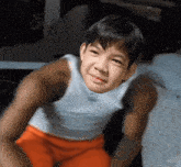 a young boy wearing orange shorts and a white tank top