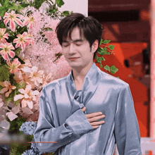a man in a blue shirt stands in front of a bouquet of flowers