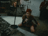 a woman with red hair is singing into a microphone in front of a drum set with the words terasgifs below her