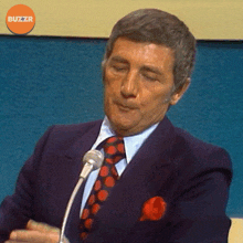 a man in a suit and tie speaking into a microphone with buzzr written on the bottom right