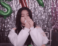 a girl is blowing her nose with a tissue in front of a green balloon with the letter s on it .