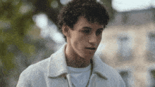a young man with curly hair is wearing a white jacket and a white t-shirt