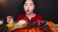 a woman in a red shirt is eating a variety of food on a table