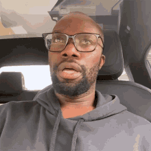 a man wearing glasses and a grey hoodie is sitting in the back seat of a car