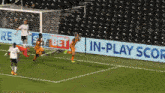 a soccer game is being played in front of an in-play score sign