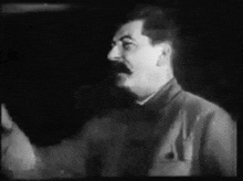 a black and white photo of a man with a mustache talking in a dark room .