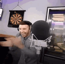 a man wearing headphones is standing in front of a microphone in front of a dart board