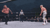 two men are wrestling in a wrestling ring and a referee is standing in the corner .