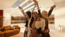 three women are dancing in a living room with their arms up in the air