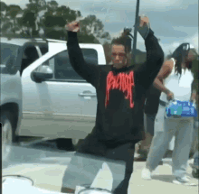 a man wearing a revenge sweatshirt is standing in front of a car