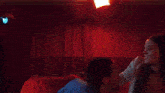 a woman is sitting on a red couch in a dark room with a red curtain .