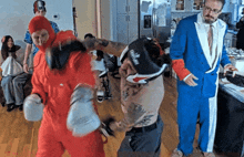 a man in a blue suit is standing next to a man in a red jumpsuit who is wearing boxing gloves