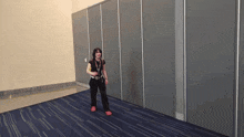 a woman is standing in a room with a blue carpet and a gray wall