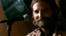 a man with a beard and long hair is sitting in front of a microphone and says " you ready "