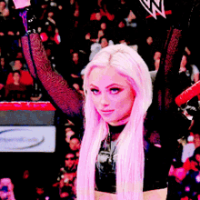 a woman with long pink hair is holding up her arms in front of a crowd