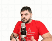 a man in a red t-shirt is sitting in front of a microphone .