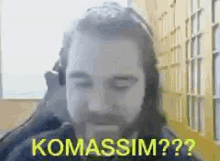 a man with a beard and headphones is sitting in front of a window and making a funny face .