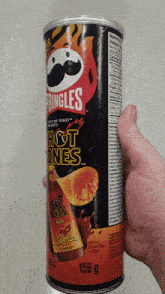 a hand is holding a can of pringles hot ones chips