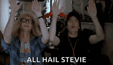 two men are sitting next to each other with their hands in the air and the words `` all hail stevie '' written above them .