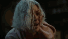 a woman with gray hair is sitting at a table with her hand on her face .
