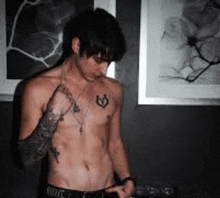 a shirtless man with a tattoo on his chest is standing in front of a wall with a picture on it .