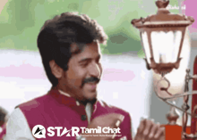 a man with a mustache is smiling in front of a star tamil chat advertisement