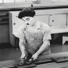 a black and white photo of a man in overalls using a grinder .