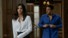 a man in a blue shirt is standing next to a woman in a white blouse
