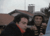 two men are standing next to a car and one is pointing