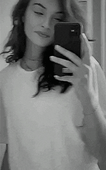 a woman is taking a selfie in a mirror with her phone .