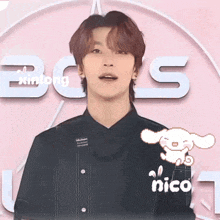 a young man in a black shirt is standing in front of a pink background with the word nico written on it .