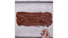 a person is using a spoon to spread chocolate on a tray .
