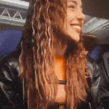 a woman with long curly hair is smiling while wearing a black leather jacket .