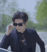 a man wearing sunglasses and a suit is standing next to a car