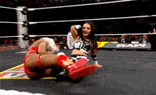 two women are wrestling in a wrestling ring and one is laying on the ground .