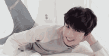 a young man is laying on his stomach on a bed with his legs crossed and smiling .