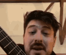 a man with a beard is playing a guitar and making a funny face .