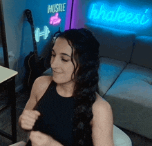 a woman is sitting in front of a neon sign that says hustle and grind