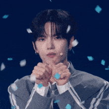 a young man is making a heart shape with his hands and feathers are falling around him