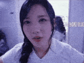a girl in a white shirt is looking at the camera with korean writing behind her